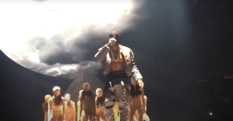 Kanye sur scène pendant le Yeezus Tour, portant un masque de cristaux et se tenant sur une scène apocalyptique devant ses danseuses
